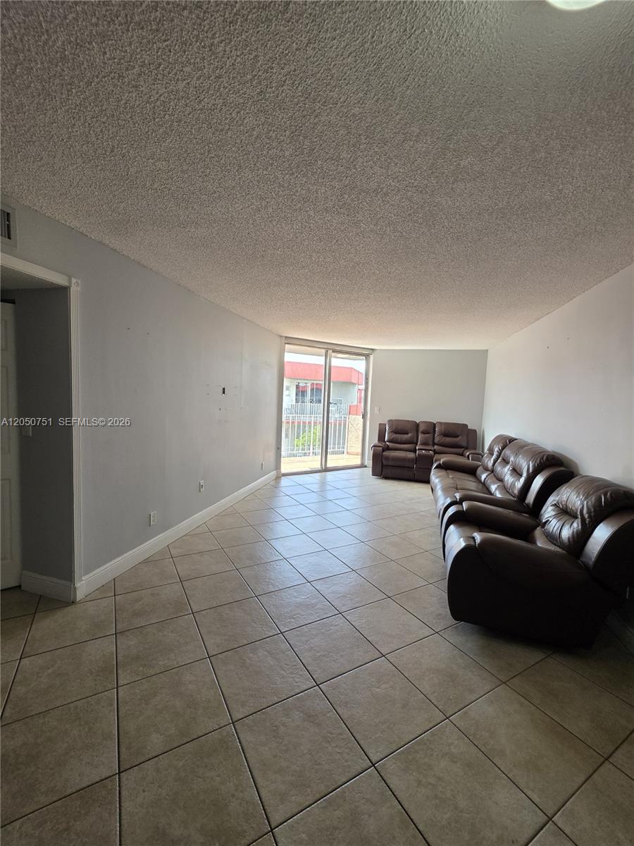 A living room features light gray walls, tile flooring, a popcorn ceiling, and brown leather sofas — 1750 W 46th St # 520, Hialeah FL 33012, HIALEAH, FL