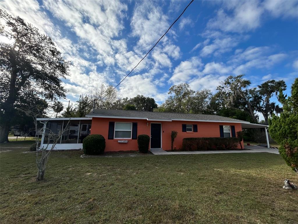 A single-story orange house with a screened-in porch and a carport under a blue sky — 1122 VIRGINIA COURT, EUSTIS, FL