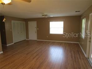 An interior view of a living room with light wood flooring, tan walls, and a ceiling fan — 1122 VIRGINIA COURT, EUSTIS, FL