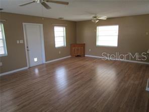 A spacious living room with light wood-look flooring, tan walls, two ceiling fans, and windows — 1122 VIRGINIA COURT, EUSTIS, FL
