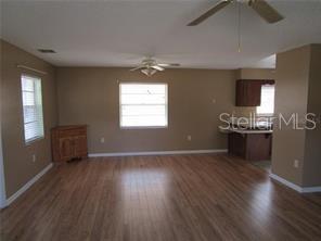 An open living area features wood-look flooring, tan walls, two ceiling fans, and a kitchen corner — 1122 VIRGINIA COURT, EUSTIS, FL