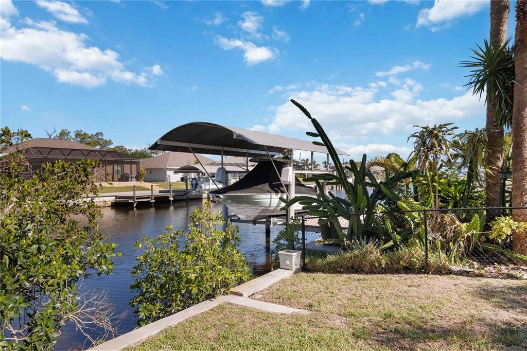 A boat under a covered lift sits in a canal behind a residential backyard — 5281 BOYLE TERRACE, PORT CHARLOTTE, FL