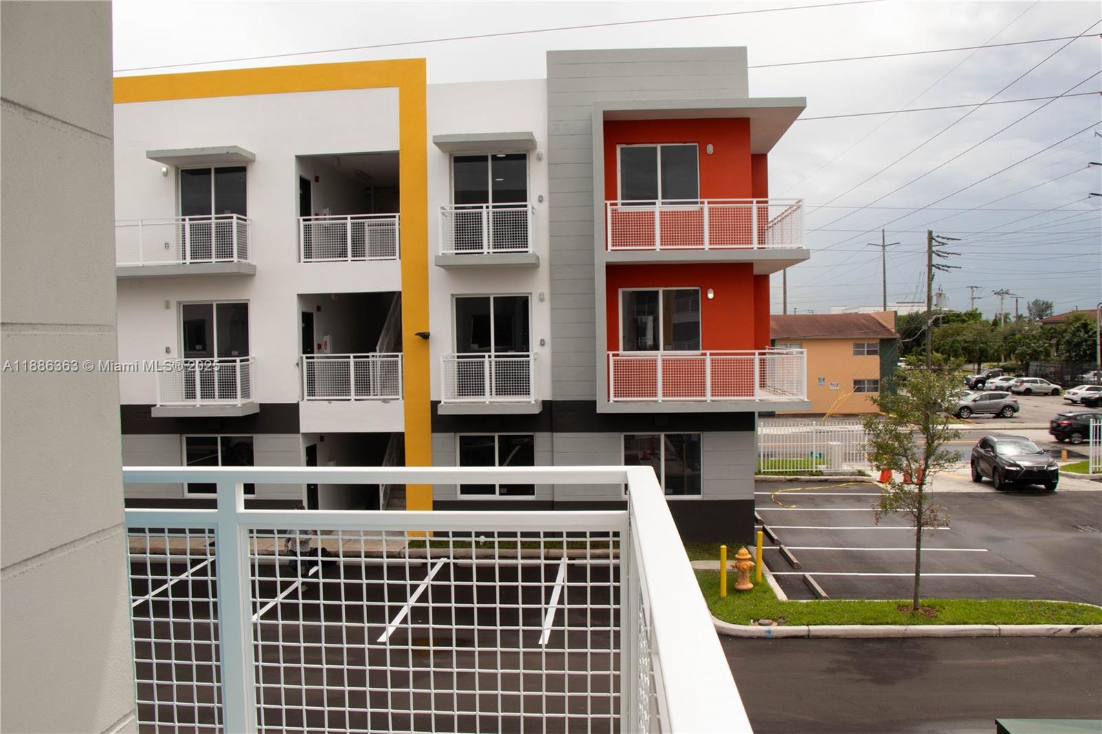 A view from a balcony looking toward a modern apartment building with parking spaces — 1455 W 29th St # 113, Hialeah FL 33012, HIALEAH, FL
