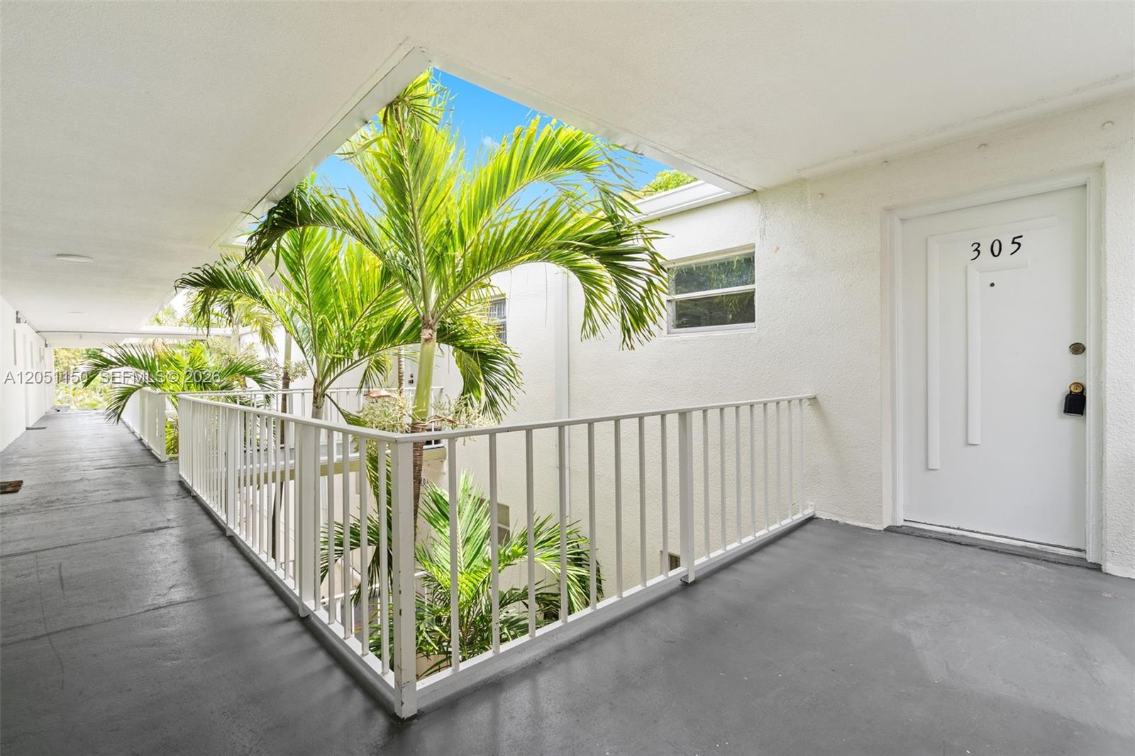 An outdoor apartment hallway features a white door labeled 305, white railings, and palm trees — 4215 N University Dr # 305, Sunrise FL 33351, SUNRISE, FL