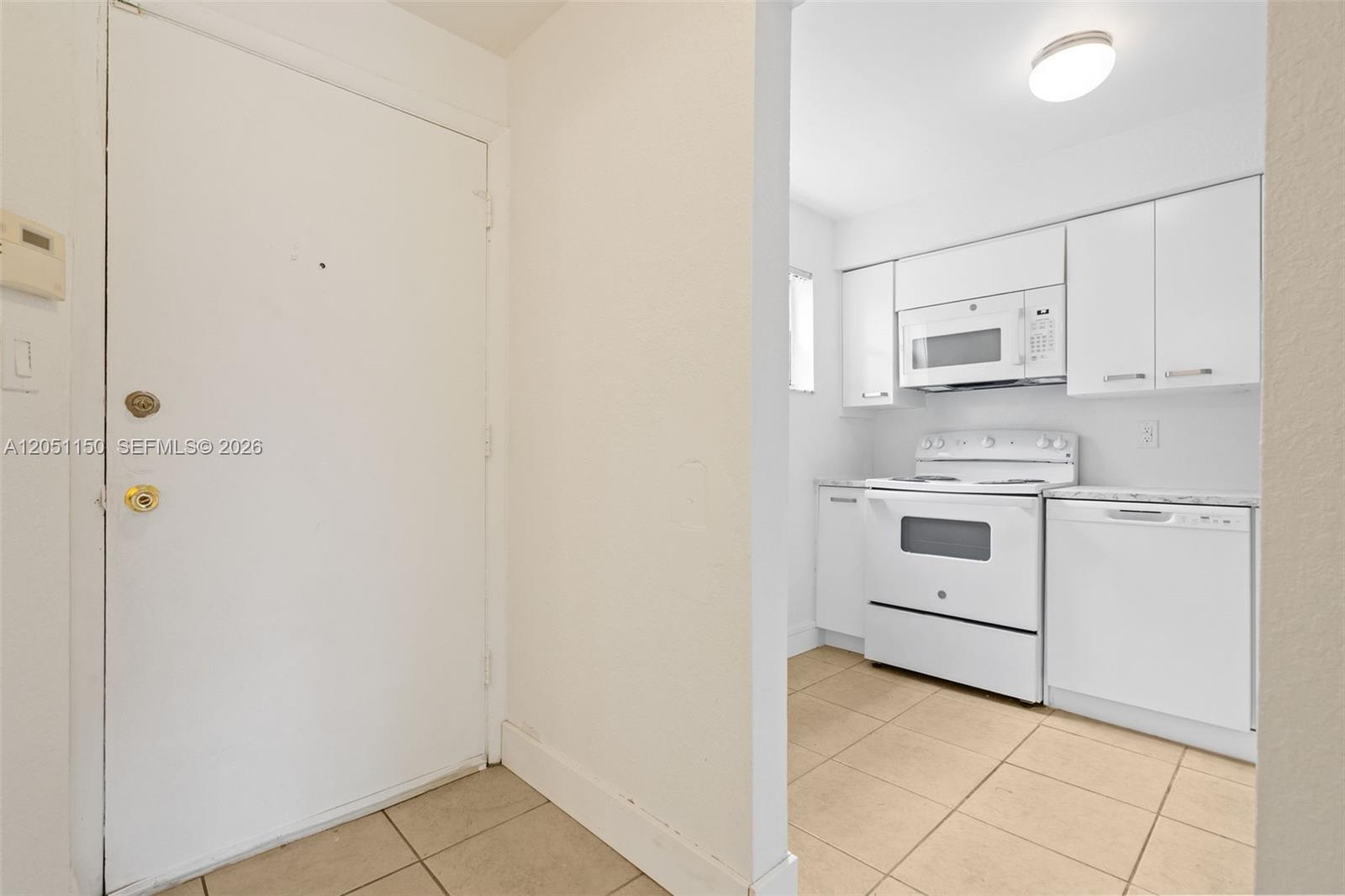 A white door opens into a kitchen featuring white cabinets, white appliances, and tiled floors — 4215 N University Dr # 305, Sunrise FL 33351, SUNRISE, FL