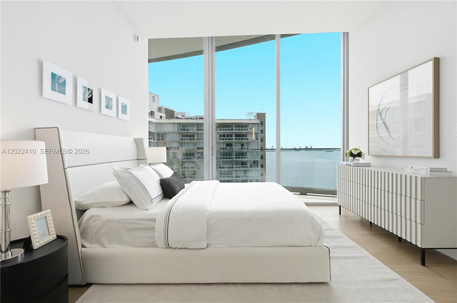 A modern bedroom features a white bed, a textured dresser, and floor-to-ceiling windows overlooking water — 175 SE 25th Rd # 1604, Miami FL 33129, MIAMI, FL