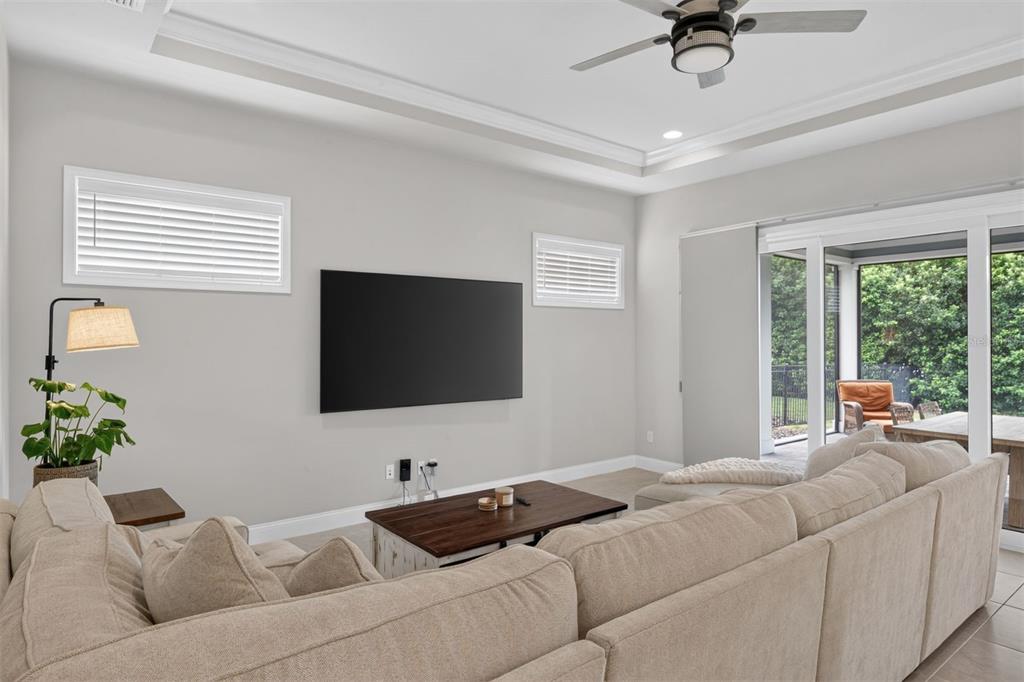 A living room features a wall-mounted television, a beige sectional sofa, and sliding glass doors — 11951 SW 32ND LANE, GAINESVILLE, FL