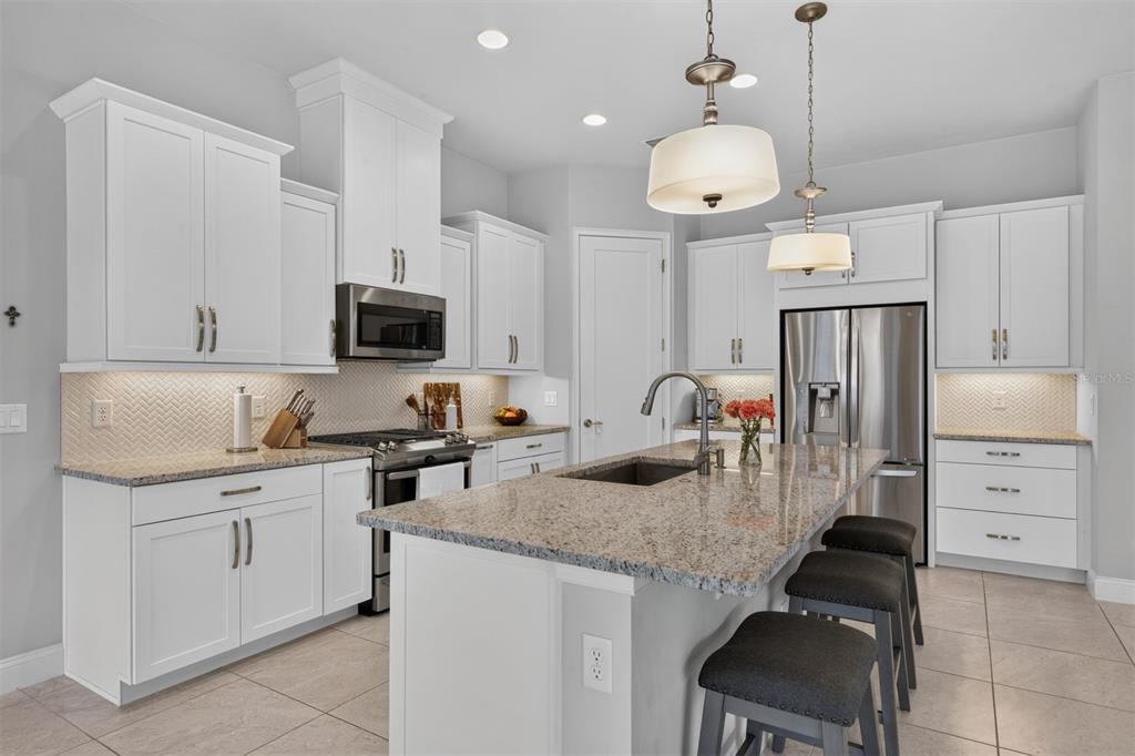 A modern kitchen features white cabinets, granite countertops, a central island, and stainless steel appliances — 11951 SW 32ND LANE, GAINESVILLE, FL