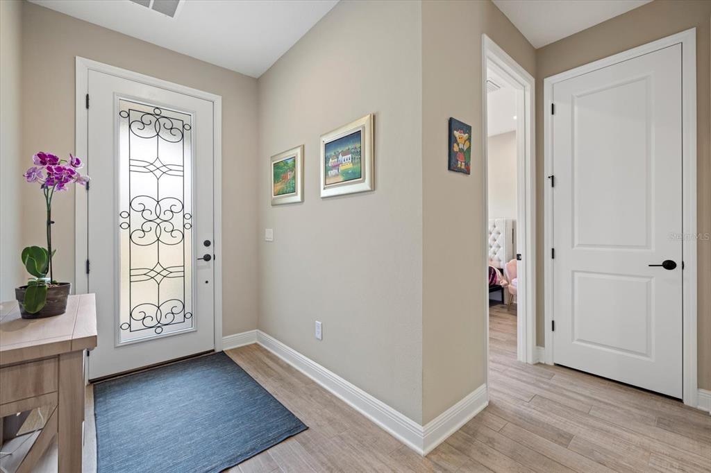 An entryway features a glass-paneled front door, light wood flooring, and two framed wall pictures — 16750 SAVORY MIST CIRCLE, BRADENTON, FL