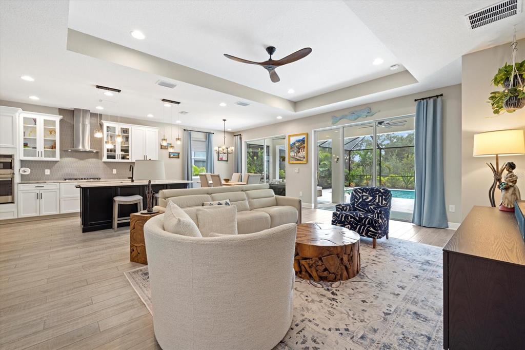 An open-concept living room and kitchen feature light-colored tile floors, a coffered ceiling, and pool views — 16750 SAVORY MIST CIRCLE, BRADENTON, FL