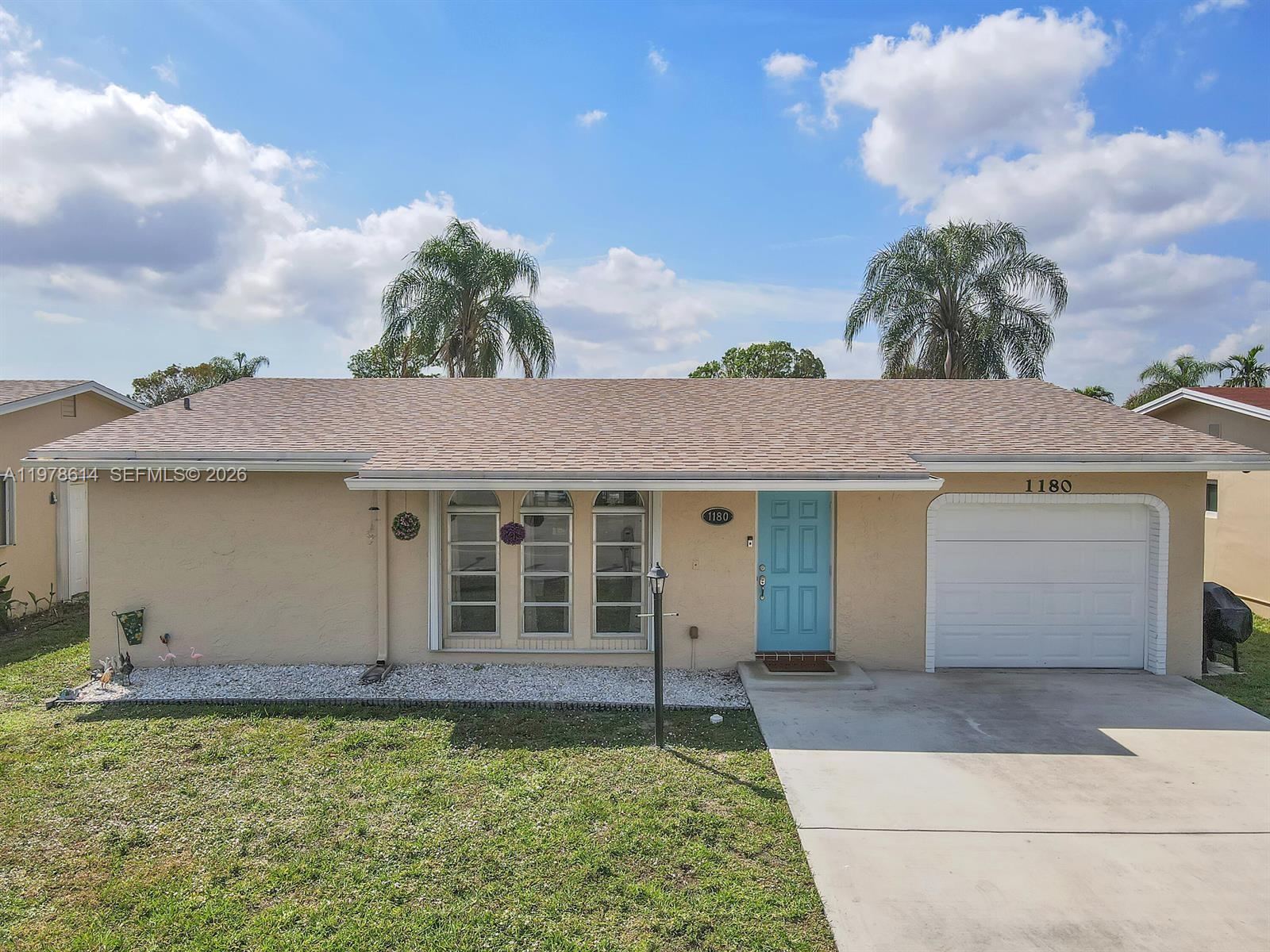 A single-story house with a tan stucco exterior, a blue front door, and a garage — 1180 NW 49th Ct, Deerfield Beach FL 33064, DEERFIELD BEACH, FL