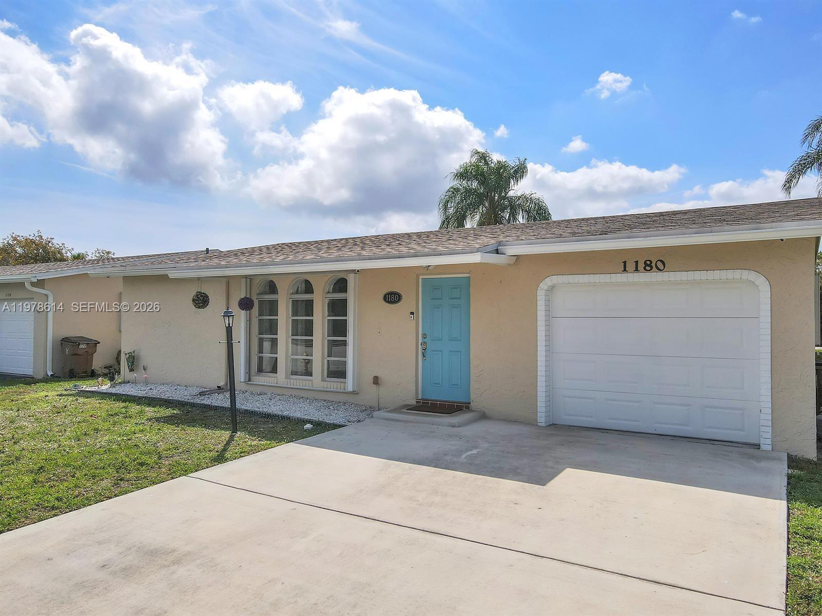 A single-story house features a light-colored stucco exterior, a blue front door, and a garage — 1180 NW 49th Ct, Deerfield Beach FL 33064, DEERFIELD BEACH, FL