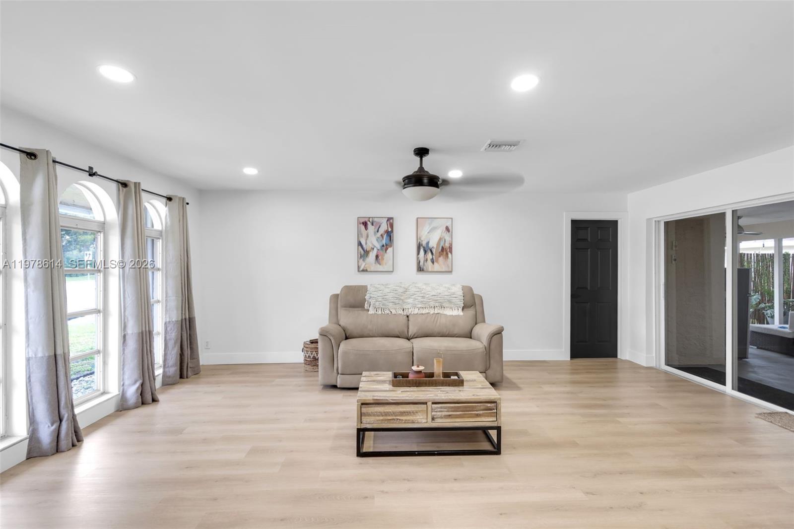A living room features light wood flooring, a beige sofa, and a black door — 1180 NW 49th Ct, Deerfield Beach FL 33064, DEERFIELD BEACH, FL