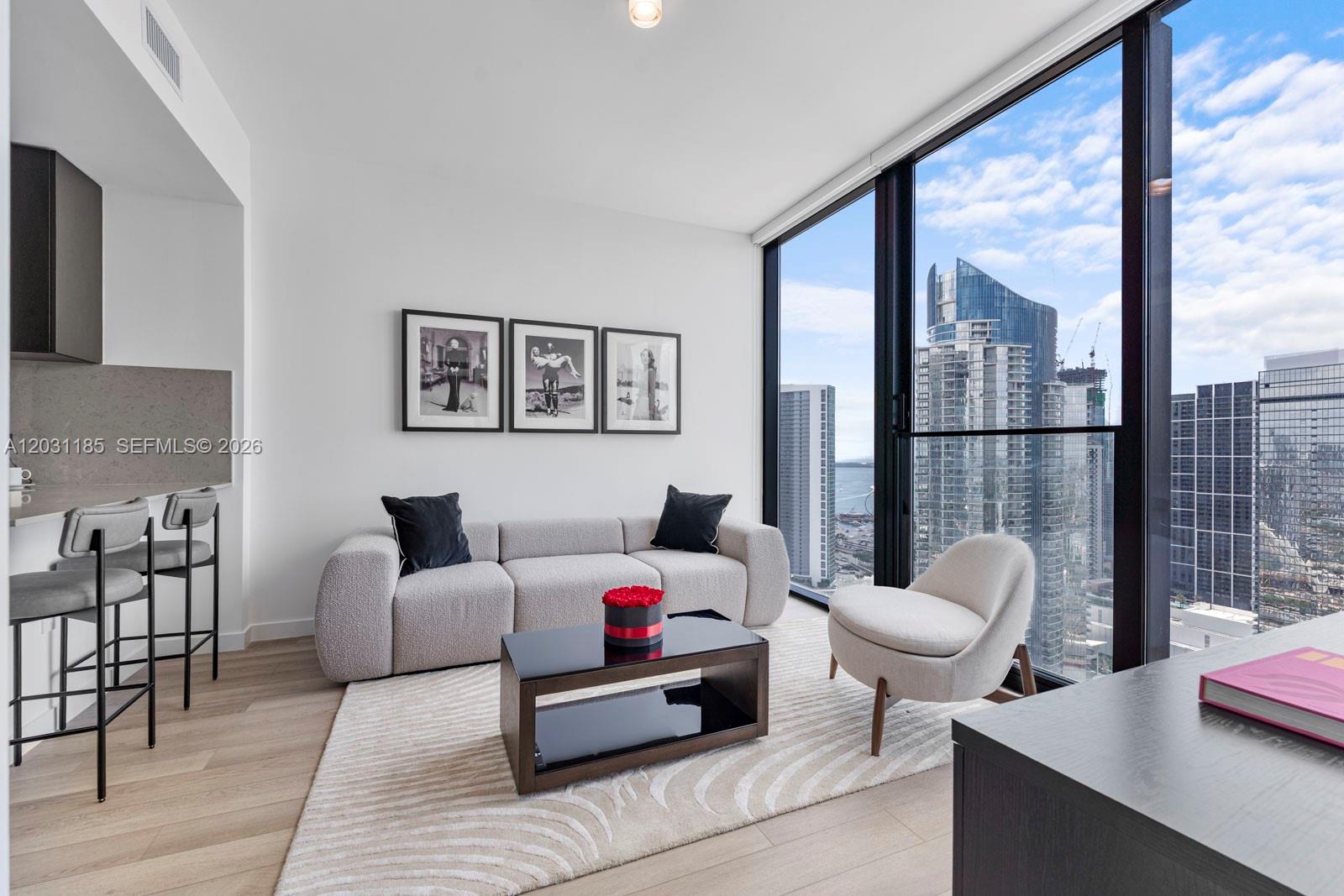 A modern living room features a grey sofa, coffee table, and floor-to-ceiling windows with city views — 20 NE 11th Street # 4309, Miami FL 33132, MIAMI, FL