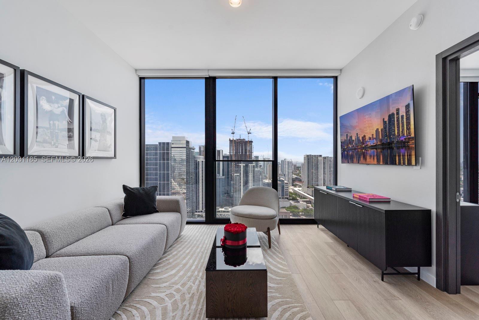 A modern living room features a grey sofa, a coffee table, and floor-to-ceiling city views — 20 NE 11th Street # 4309, Miami FL 33132, MIAMI, FL