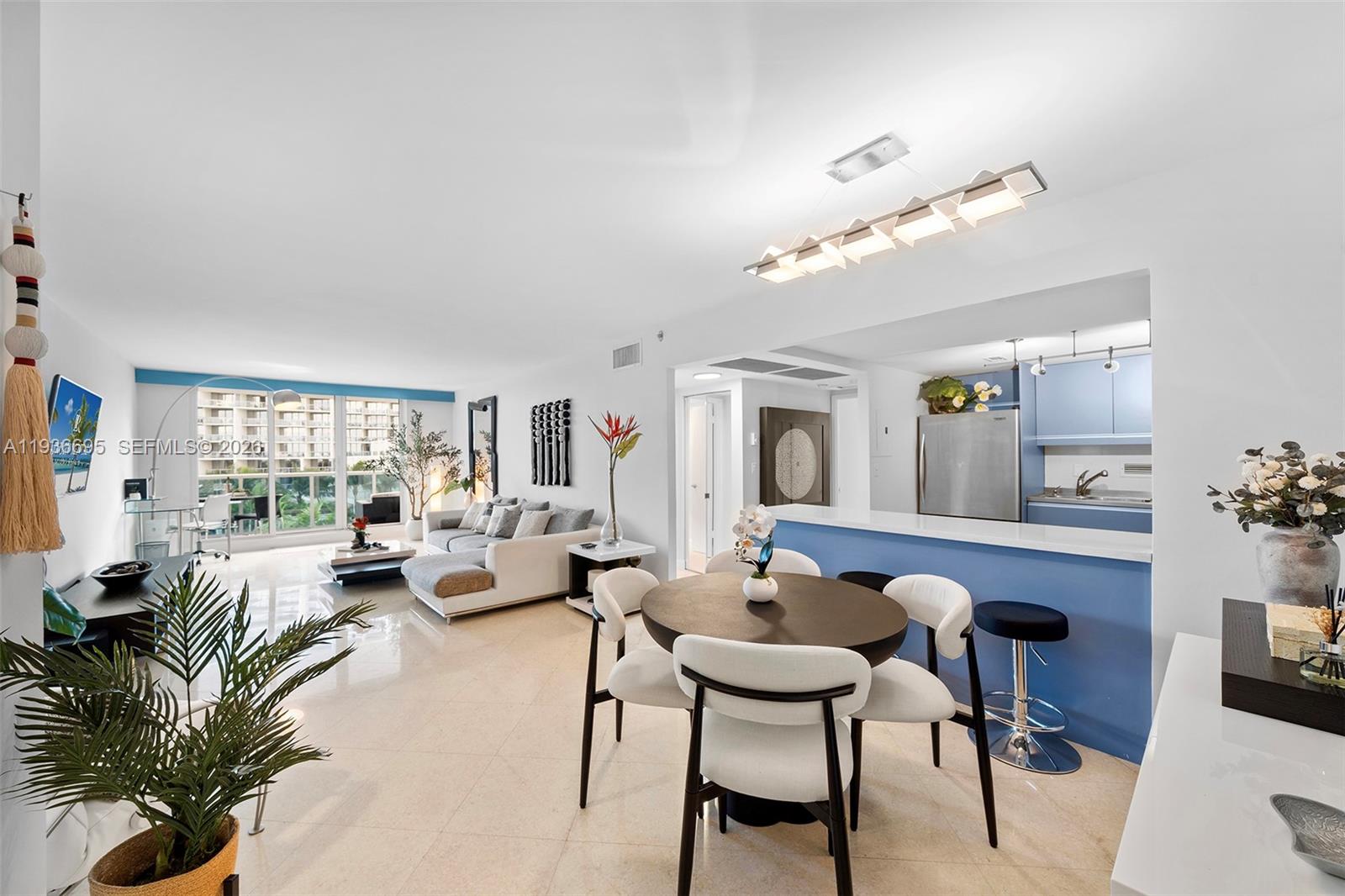 An open-concept living and dining area features white tile floors, a blue kitchen island, and balcony — 2301 Collins Ave # 408, Miami Beach FL 33139, MIAMI BEACH, FL