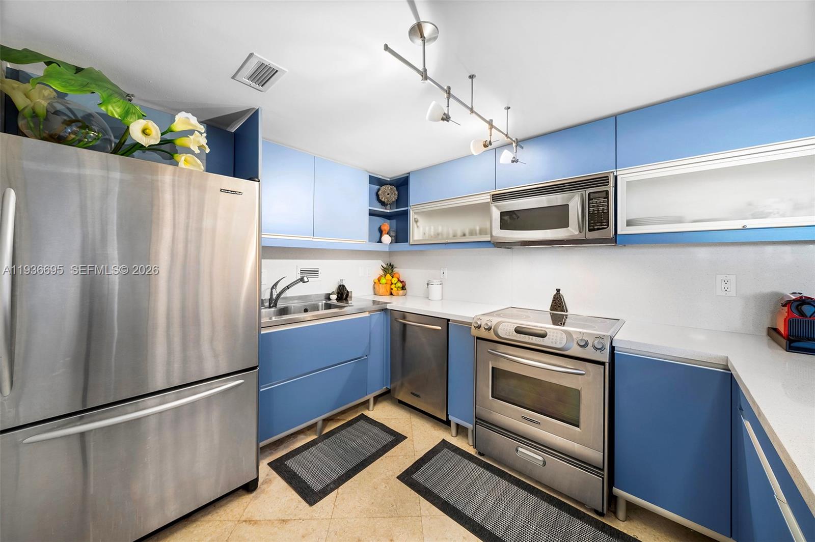 A kitchen features blue cabinets, stainless steel appliances, and light-colored countertops — 2301 Collins Ave # 408, Miami Beach FL 33139, MIAMI BEACH, FL