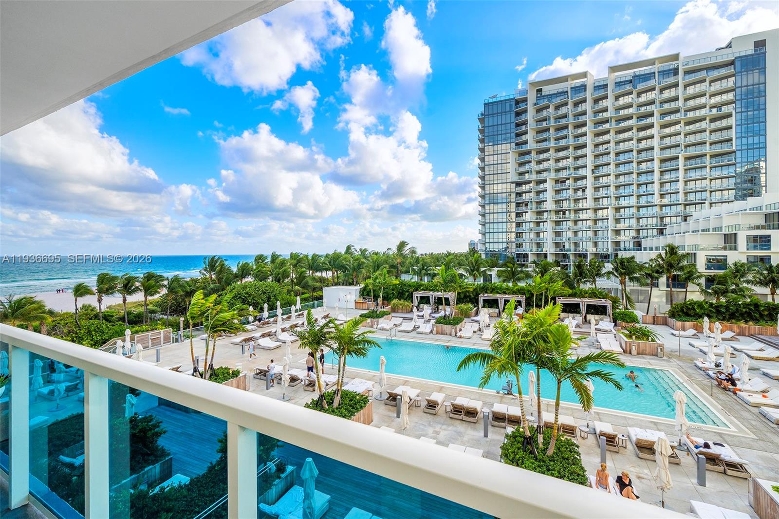 A balcony view overlooks a swimming pool, palm trees, and the ocean near a high-rise building — 2301 Collins Ave # 408, Miami Beach FL 33139, MIAMI BEACH, FL