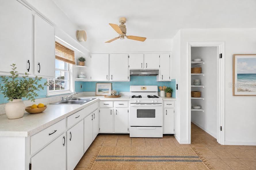 A kitchen features white cabinets, a blue tiled backsplash, a white stove, and a pantry — 1700 COWAN CIRCLE, TITUSVILLE, FL