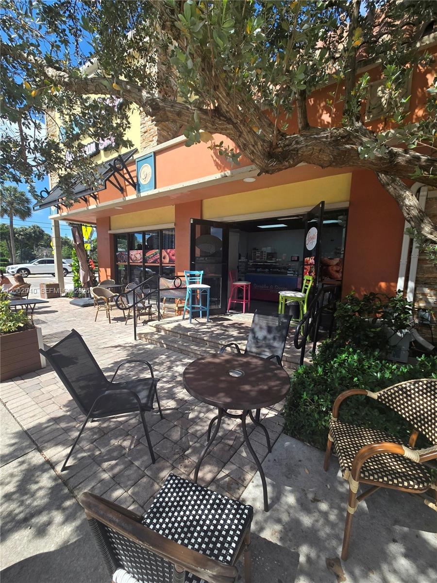An outdoor patio area features several tables and chairs in front of a storefront entrance — 899 E PALMETTO PARK RD, Boca Raton FL 33432, BOCA RATON, FL