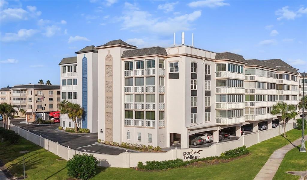 An exterior view of the Port Belleair apartment complex with covered parking and palm trees — 131 BLUFF VIEW DRIVE UNIT 109, BELLEAIR BLUFFS, FL