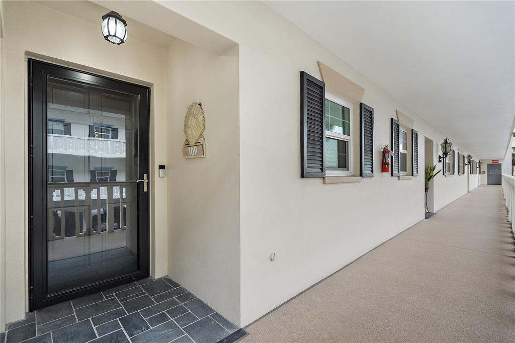 An exterior view of a building corridor featuring a front door with a storm door — 131 BLUFF VIEW DRIVE UNIT 109, BELLEAIR BLUFFS, FL