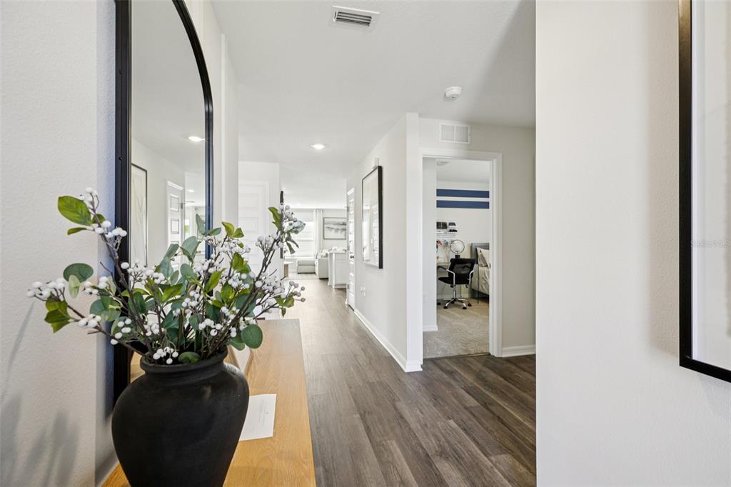A hallway with wood-look flooring leads past a side room toward a bright living area — 765 GREENWAY BOULEVARD, LAKE WALES, FL