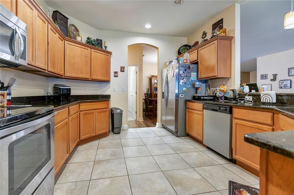 A kitchen with light wood cabinets, dark countertops, stainless steel appliances, and beige tile flooring — 2818 WHITNEY STREET, LAKELAND, FL