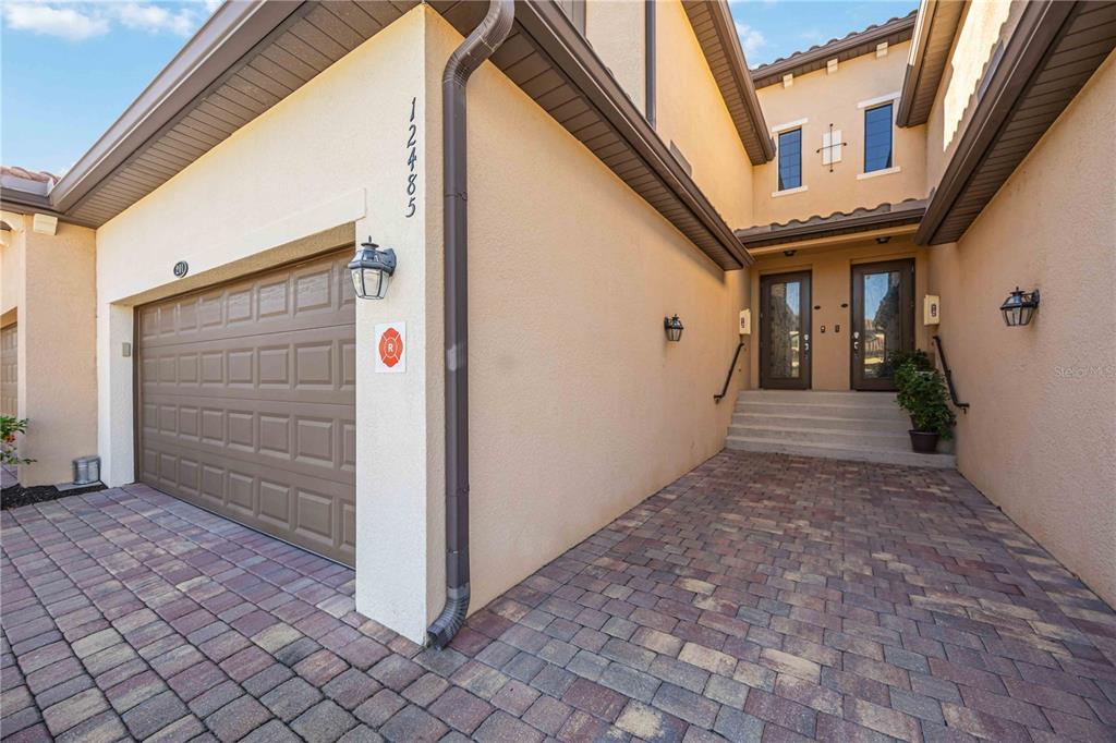 A beige stucco house exterior features a brown garage door, paver driveway, and front steps — 12485 GHIBERTI CIRCLE UNIT 201, VENICE, FL