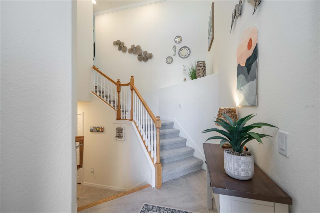 A foyer features a carpeted staircase with wood railings, tile flooring, and a console table — 12485 GHIBERTI CIRCLE UNIT 201, VENICE, FL