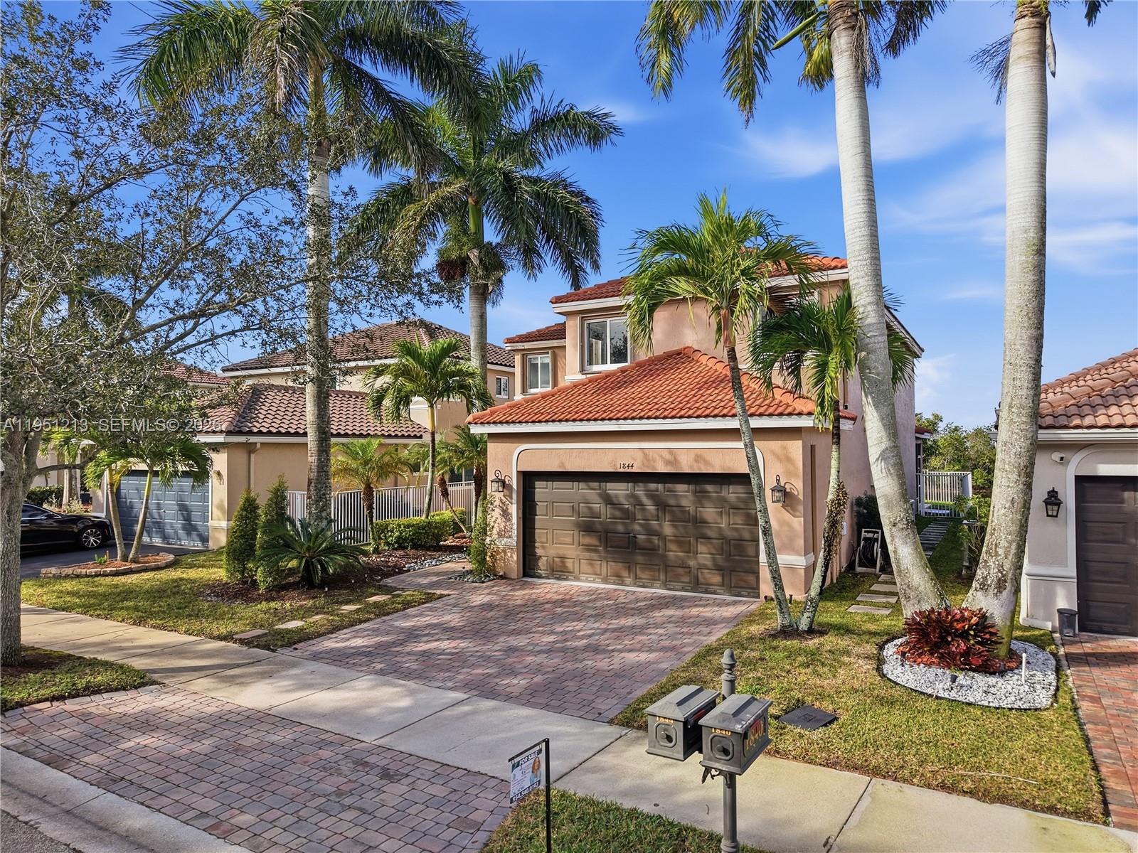 A two-story stucco house with a tile roof and a brick driveway features palm trees — 1844 Aspen Ln, Weston FL 33327, WESTON, FL
