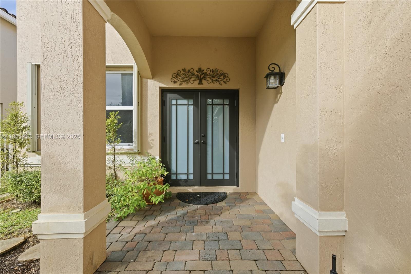 A covered entryway features a paver floor, tan stucco walls, and double glass doors — 1844 Aspen Ln, Weston FL 33327, WESTON, FL