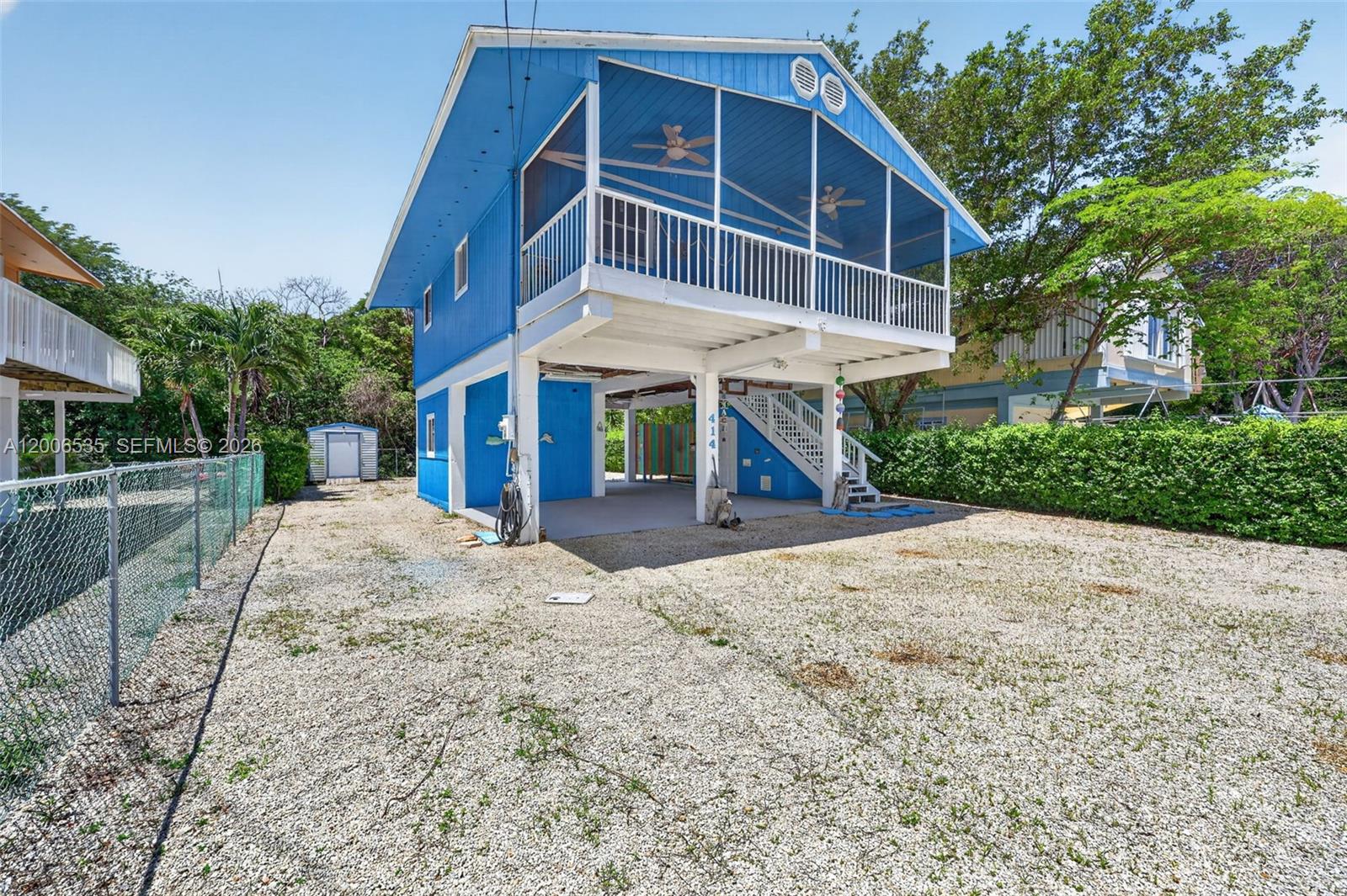 A blue elevated house features a large screened-in porch and a gravel driveway — 414 Mahogany Ave, Key Largo FL 33037, KEY LARGO, FL
