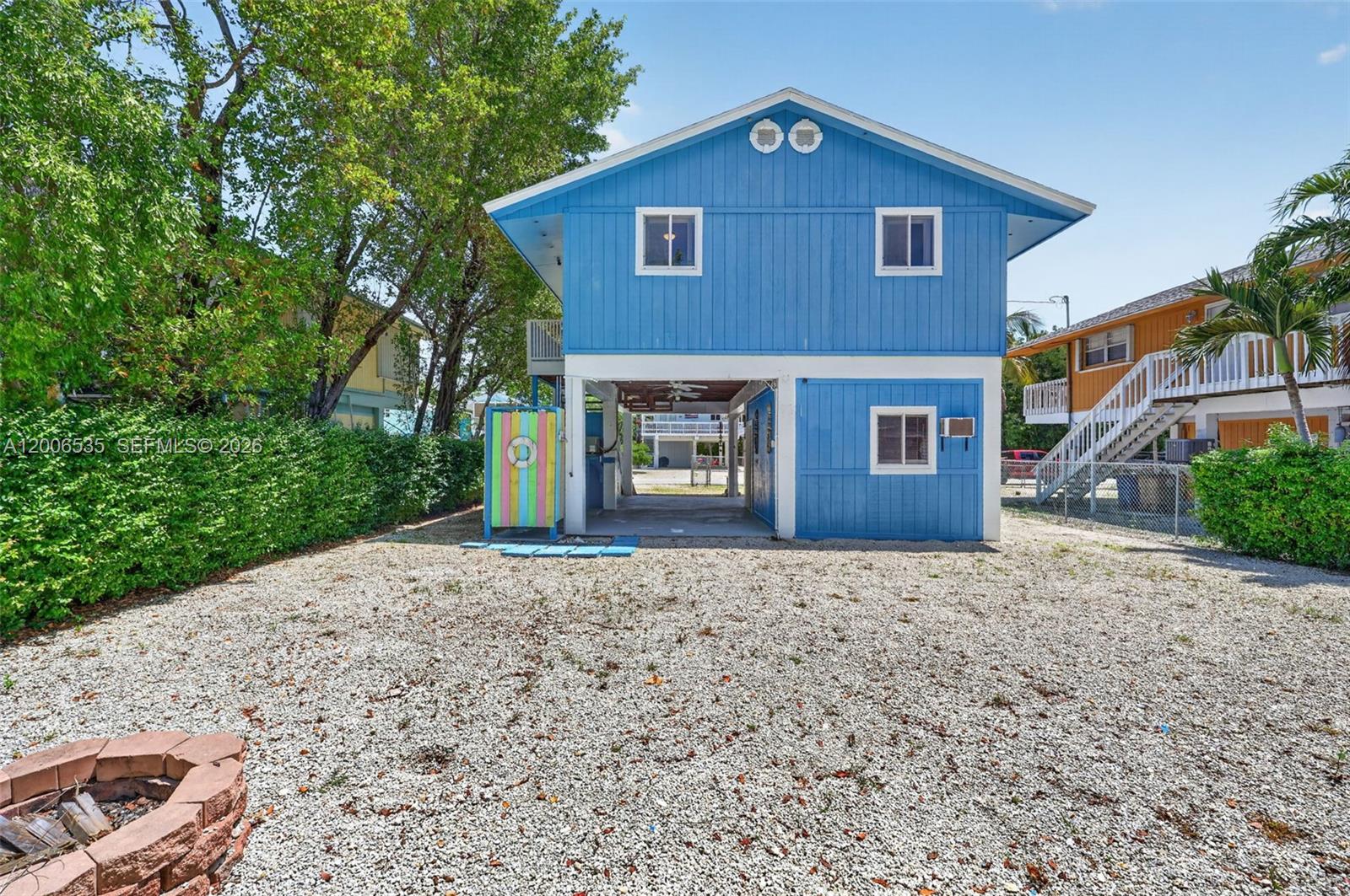 A blue two-story house stands on stilts above a gravel yard with a fire pit — 414 Mahogany Ave, Key Largo FL 33037, KEY LARGO, FL