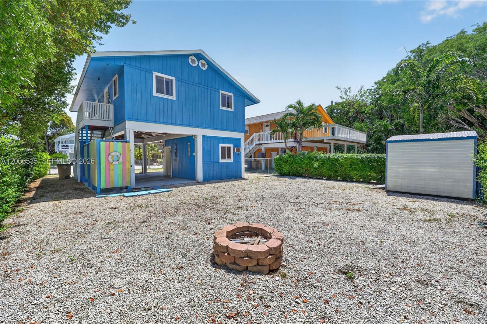A blue elevated house stands behind a gravel yard with a stone fire pit — 414 Mahogany Ave, Key Largo FL 33037, KEY LARGO, FL