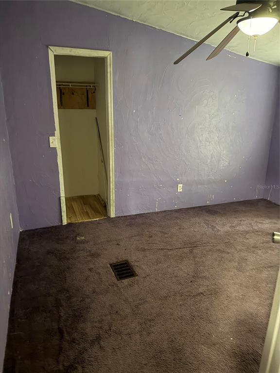 A bedroom with purple textured walls, dark carpet, a ceiling fan, and an open closet — 11455 NW 110TH AVENUE, REDDICK, FL