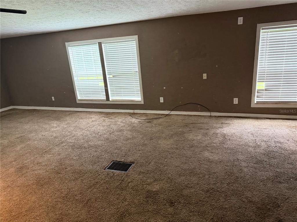 A carpeted room features brown walls, two windows with white blinds, and a floor vent — 11455 NW 110TH AVENUE, REDDICK, FL