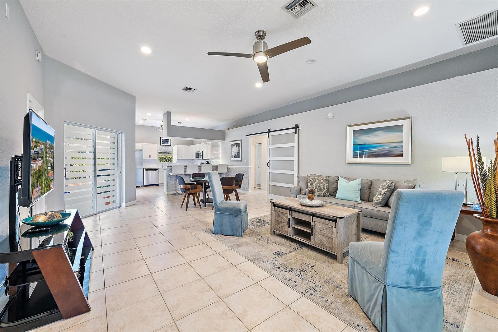 A living room with tile floors, a gray sofa, and an open kitchen in the background — 6051 Kendrick Street, Jupiter FL 33458, JUPITER, FL