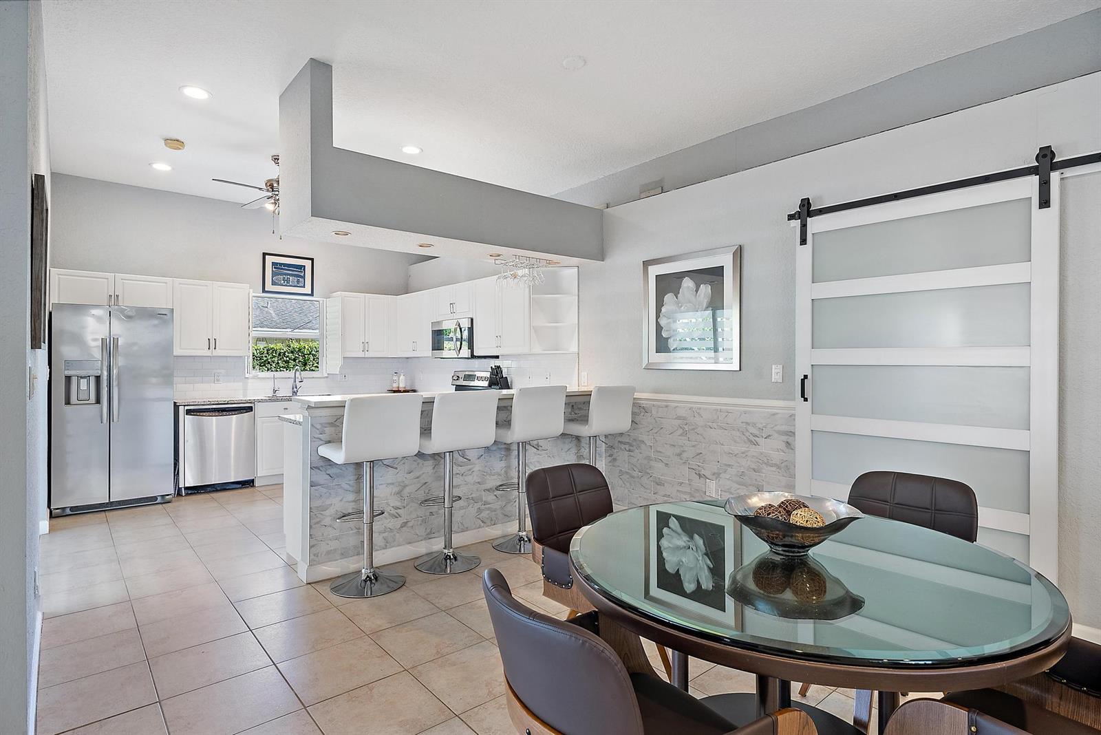 A kitchen with white cabinets and a breakfast bar overlooks a dining area with a table — 6051 Kendrick Street, Jupiter FL 33458, JUPITER, FL