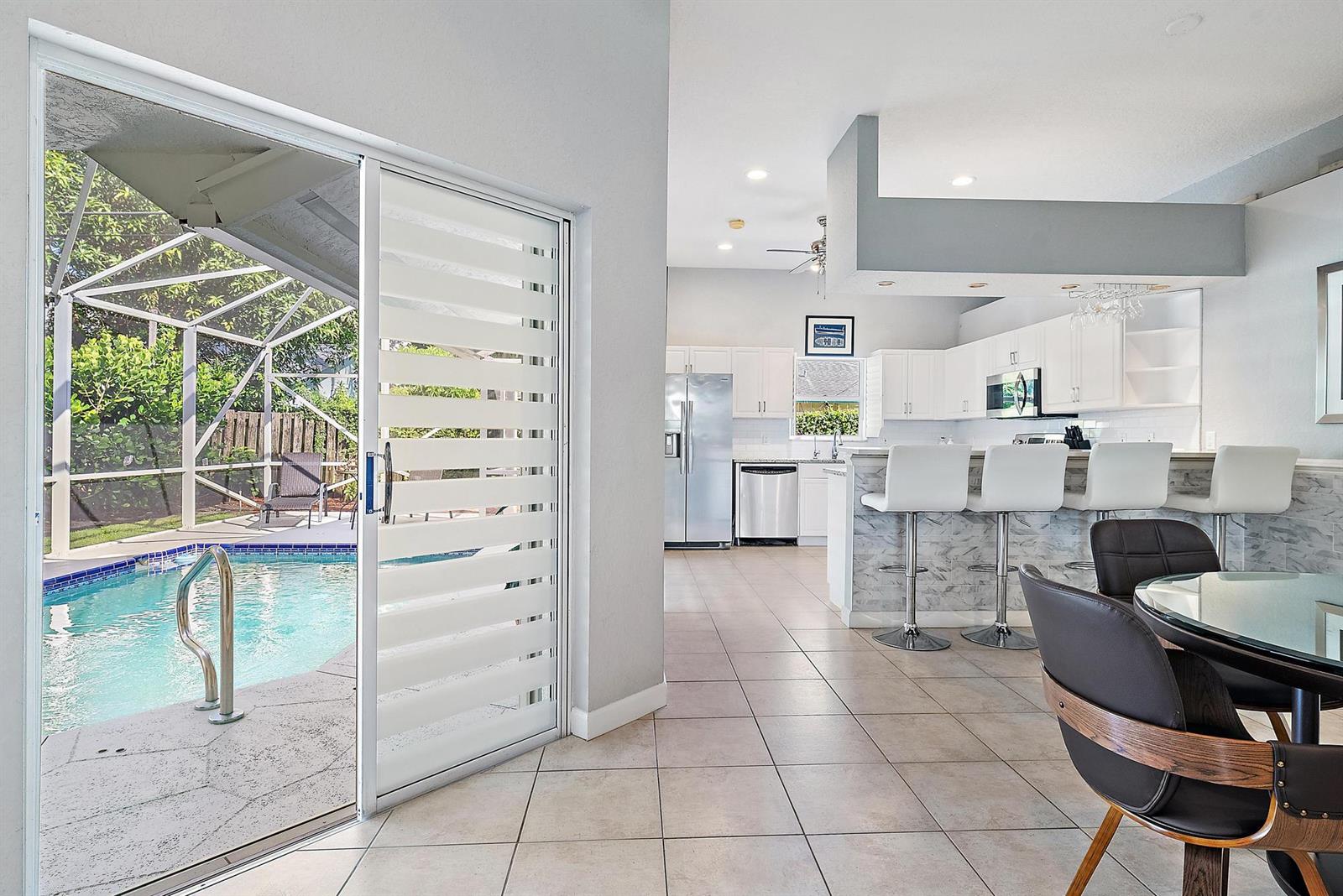 A kitchen with white cabinets and a breakfast bar overlooks a pool and patio area — 6051 Kendrick Street, Jupiter FL 33458, JUPITER, FL