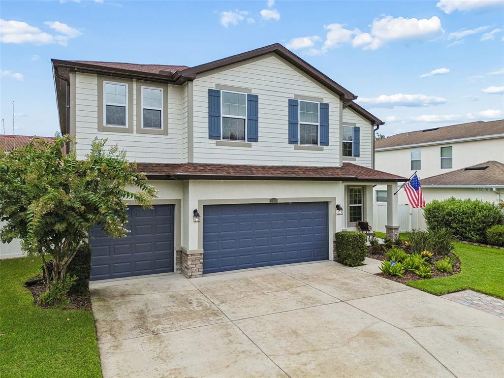 A two-story house with light siding, blue shutters, a three-car garage, and a concrete driveway — 23958 TERRACINA COURT, LAND O LAKES, FL