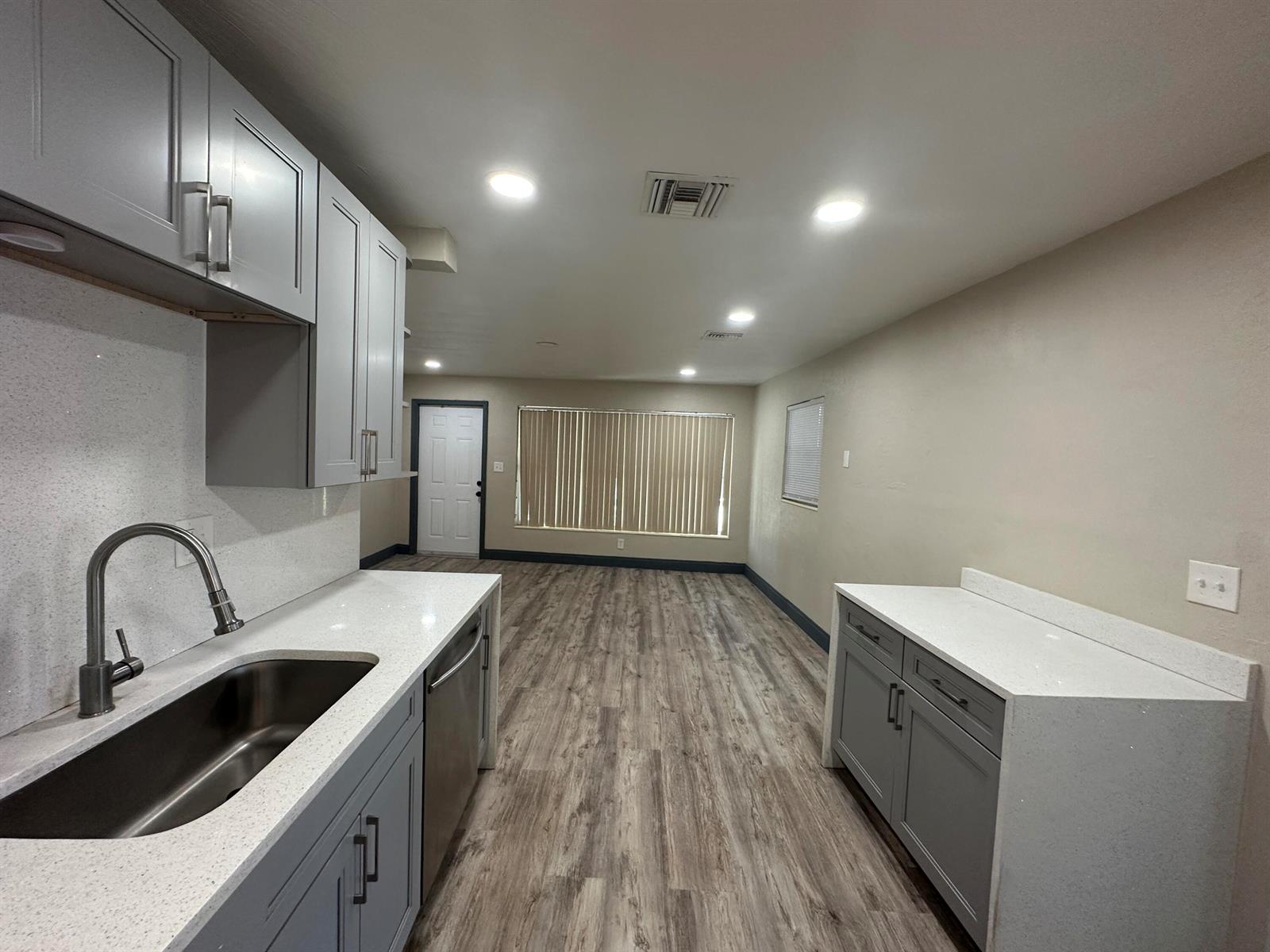 A kitchen with gray cabinets, white countertops, and wood-look flooring opens into a living area — 2550 NE 7th Terrace, Pompano Beach FL 33064, POMPANO BEACH, FL