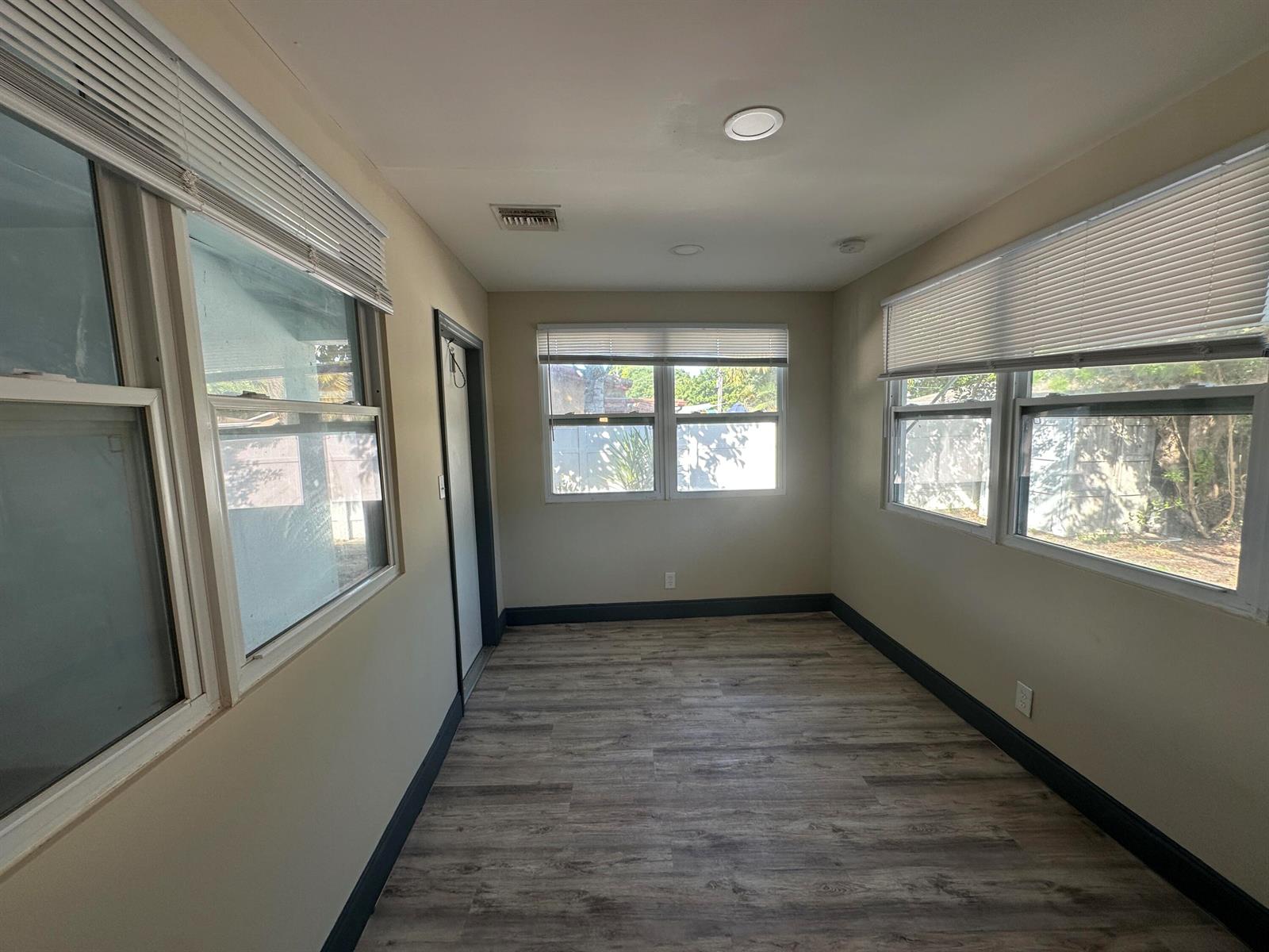 A sunroom features light-colored walls, dark baseboards, wood-look flooring, and multiple windows with blinds — 2550 NE 7th Terrace, Pompano Beach FL 33064, POMPANO BEACH, FL