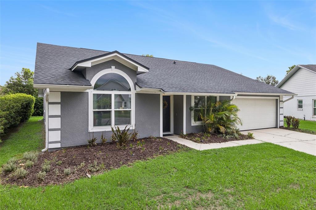 A gray single-story house with a white garage door, arched window, and landscaped front yard — 2011 EXCALIBUR DRIVE, ORLANDO, FL