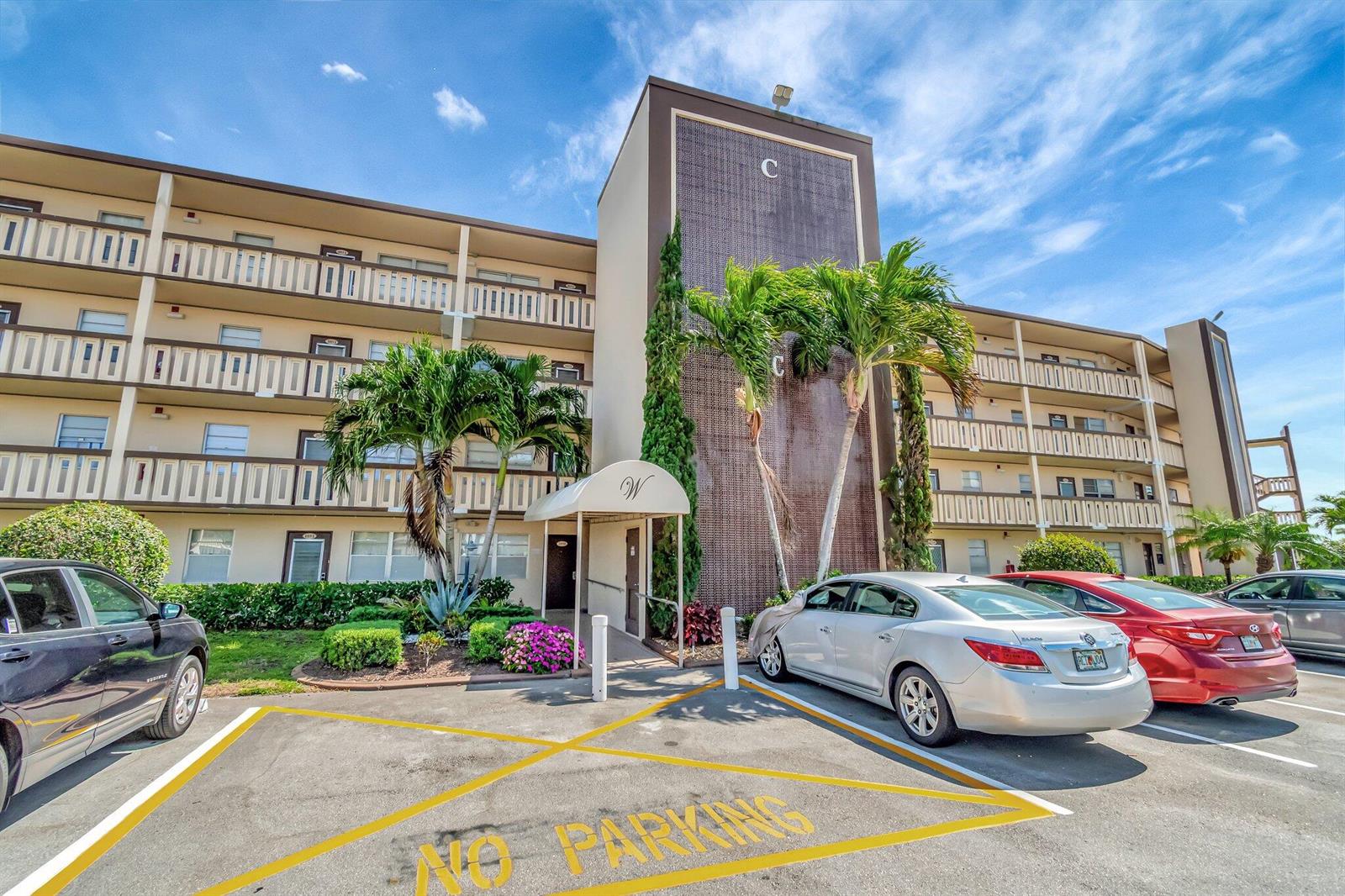 A multi-story apartment building with a central entrance, palm trees, and a parking lot — 4049 Wolverton C, Boca Raton FL 33434, BOCA RATON, FL