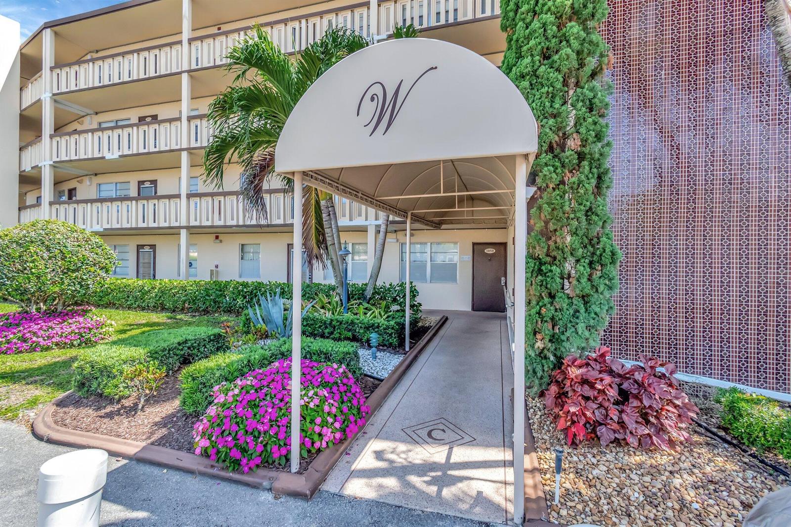 An exterior view of a building entrance with a beige awning featuring a letter W — 4049 Wolverton C, Boca Raton FL 33434, BOCA RATON, FL