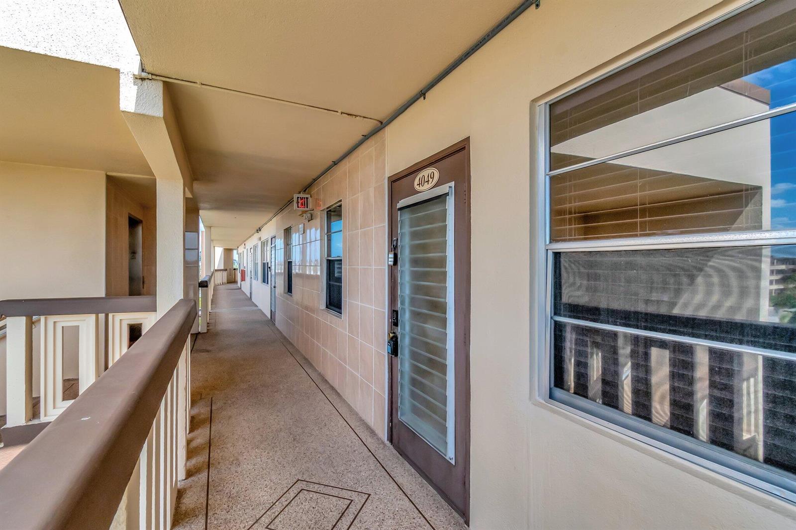 An outdoor apartment building walkway with a numbered door and large windows — 4049 Wolverton C, Boca Raton FL 33434, BOCA RATON, FL