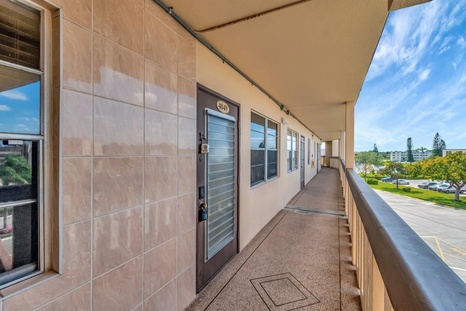 An exterior apartment walkway features a tiled wall, a door numbered 4049, and railings — 4049 Wolverton C, Boca Raton FL 33434, BOCA RATON, FL