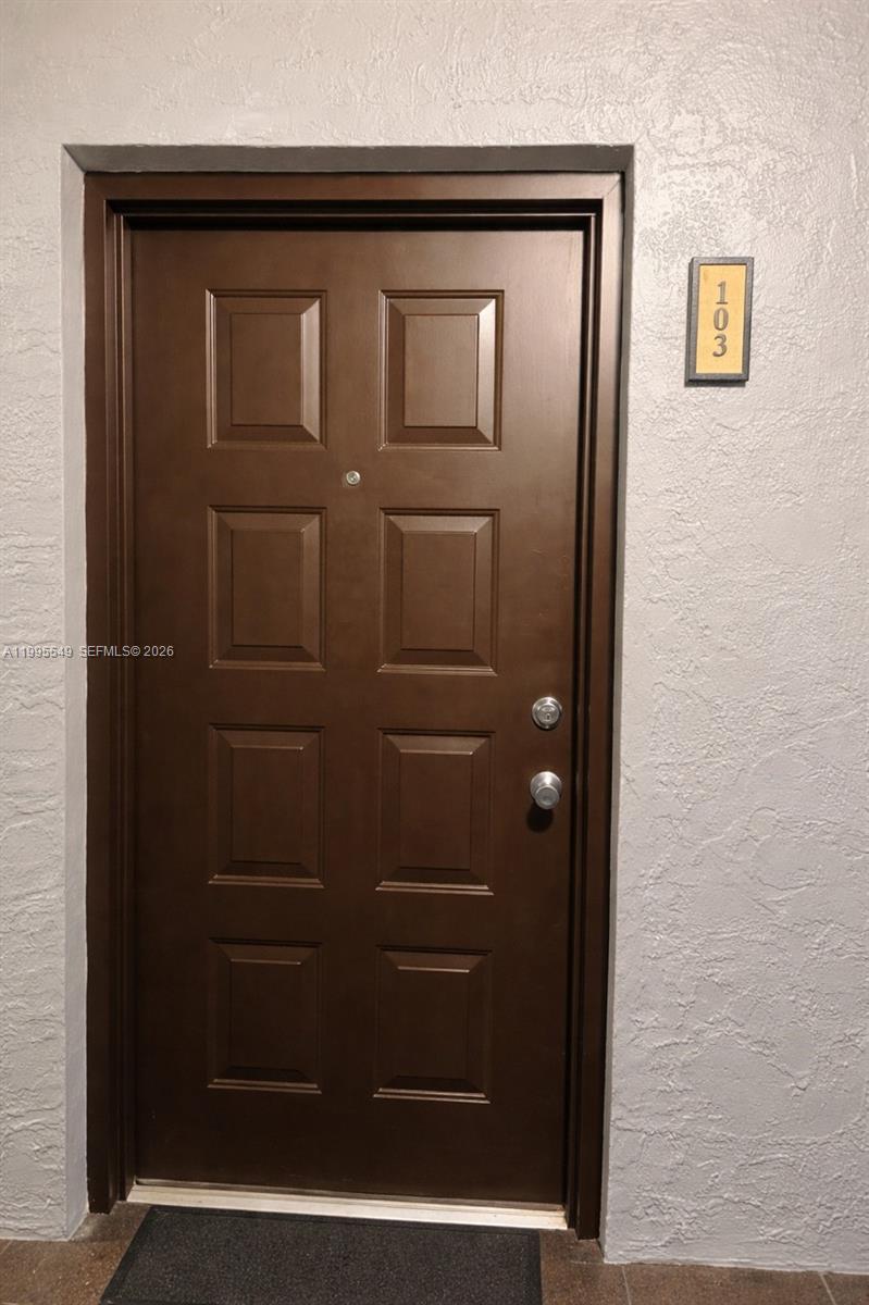A brown six-panel door with a silver peephole and hardware is labeled with number 103 — 7423 SW 152ND AVE # 103, Miami FL 33193, MIAMI, FL