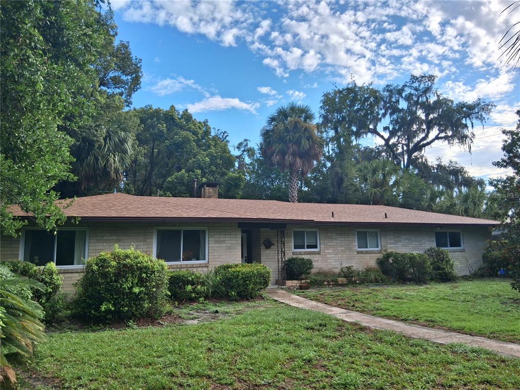 A single-story brick house with a brown shingled roof sits behind a grassy front yard — 1326 NW 14TH AVENUE, GAINESVILLE, FL